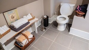 A bathroom with a toilet, a sink, and a shelf with towels and baskets. - Guest House of Kentucky (2 Singles - 2nd Floor) (Lancaster)