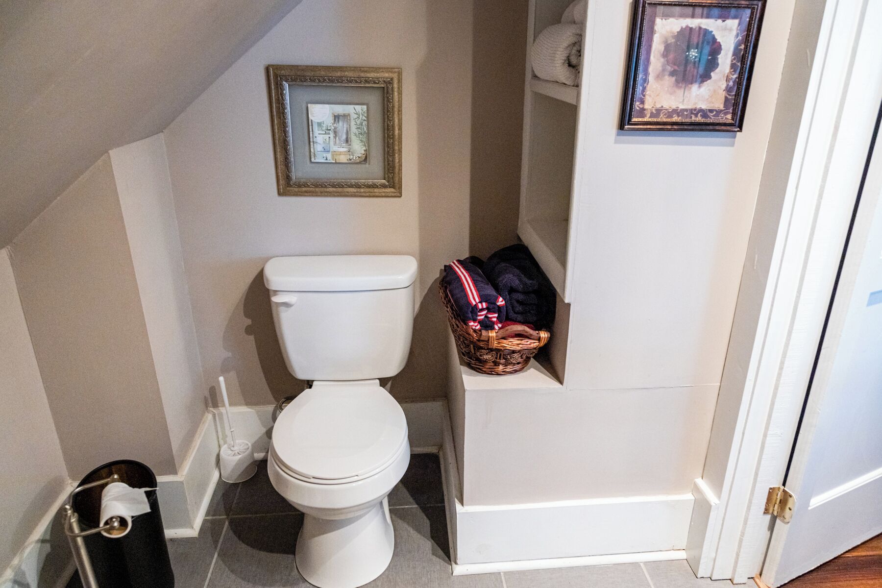 Een kleine badkamer met een toilet, een prullenbak en een rieten mand op de vloer.