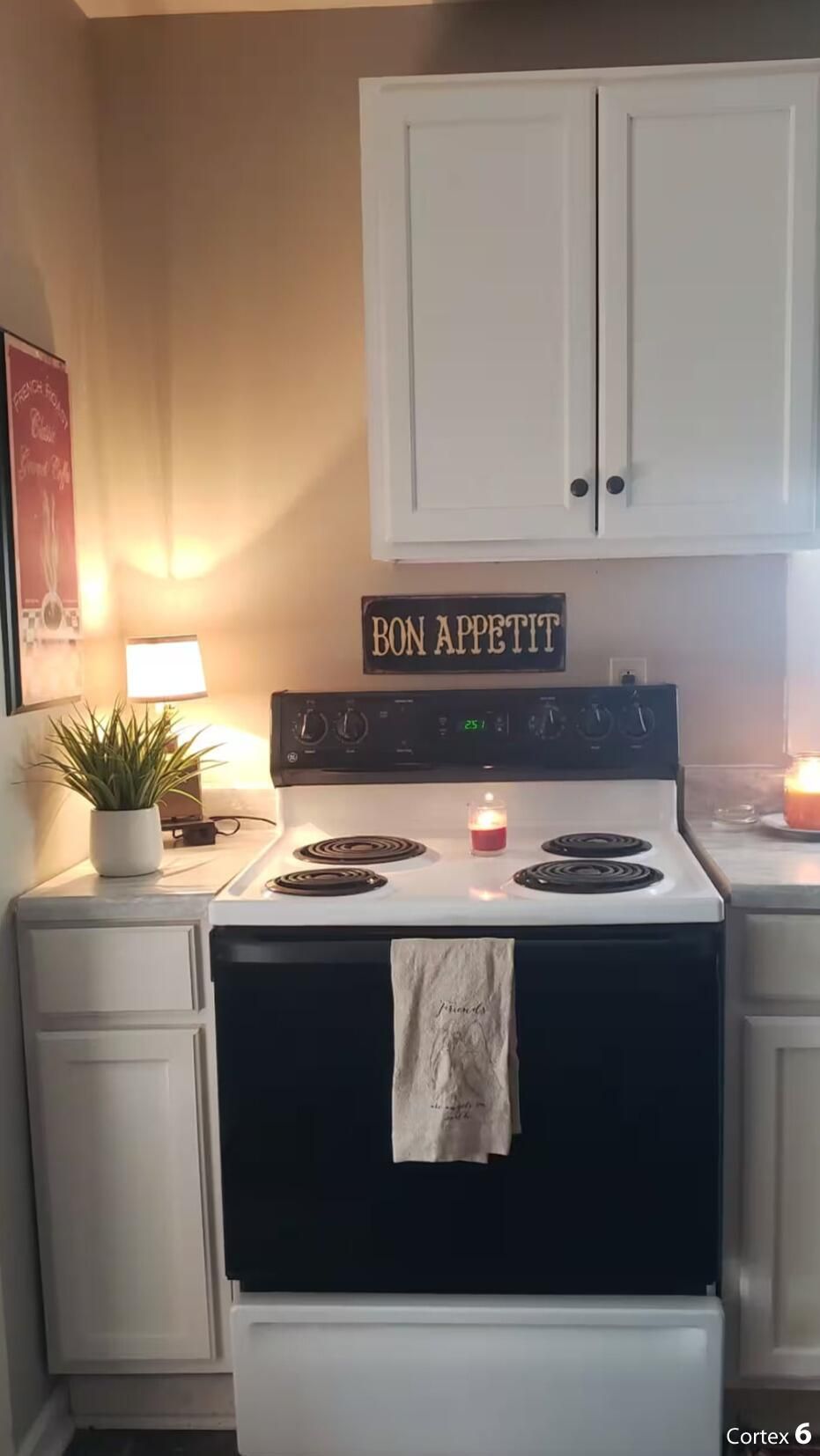 Una cocina con estufa, armarios, un cartel que dice "BON APPETIT", una planta y una vela.