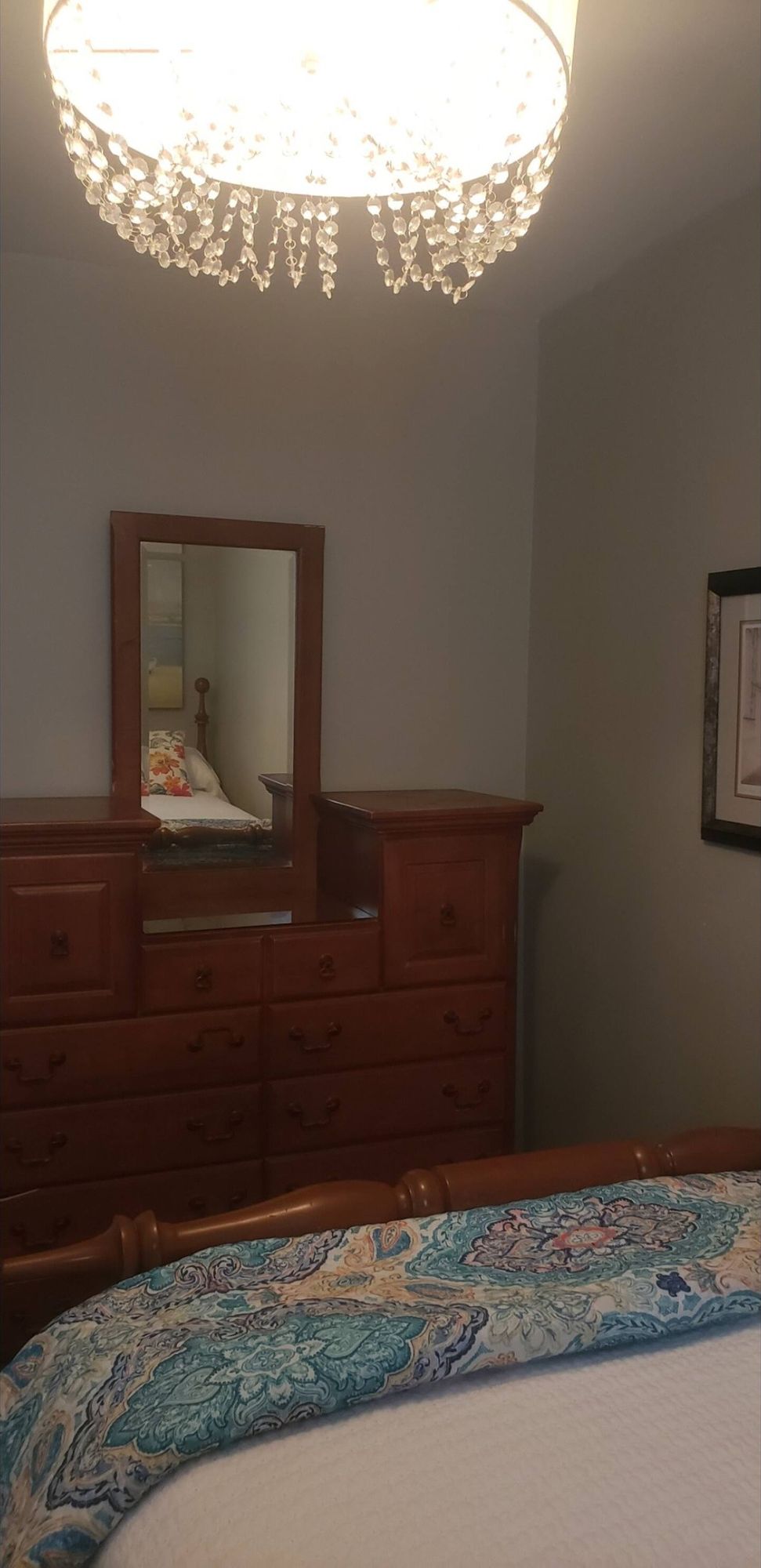 Una camera da letto con un letto, una cassettiera in legno, uno specchio e un lampadario.