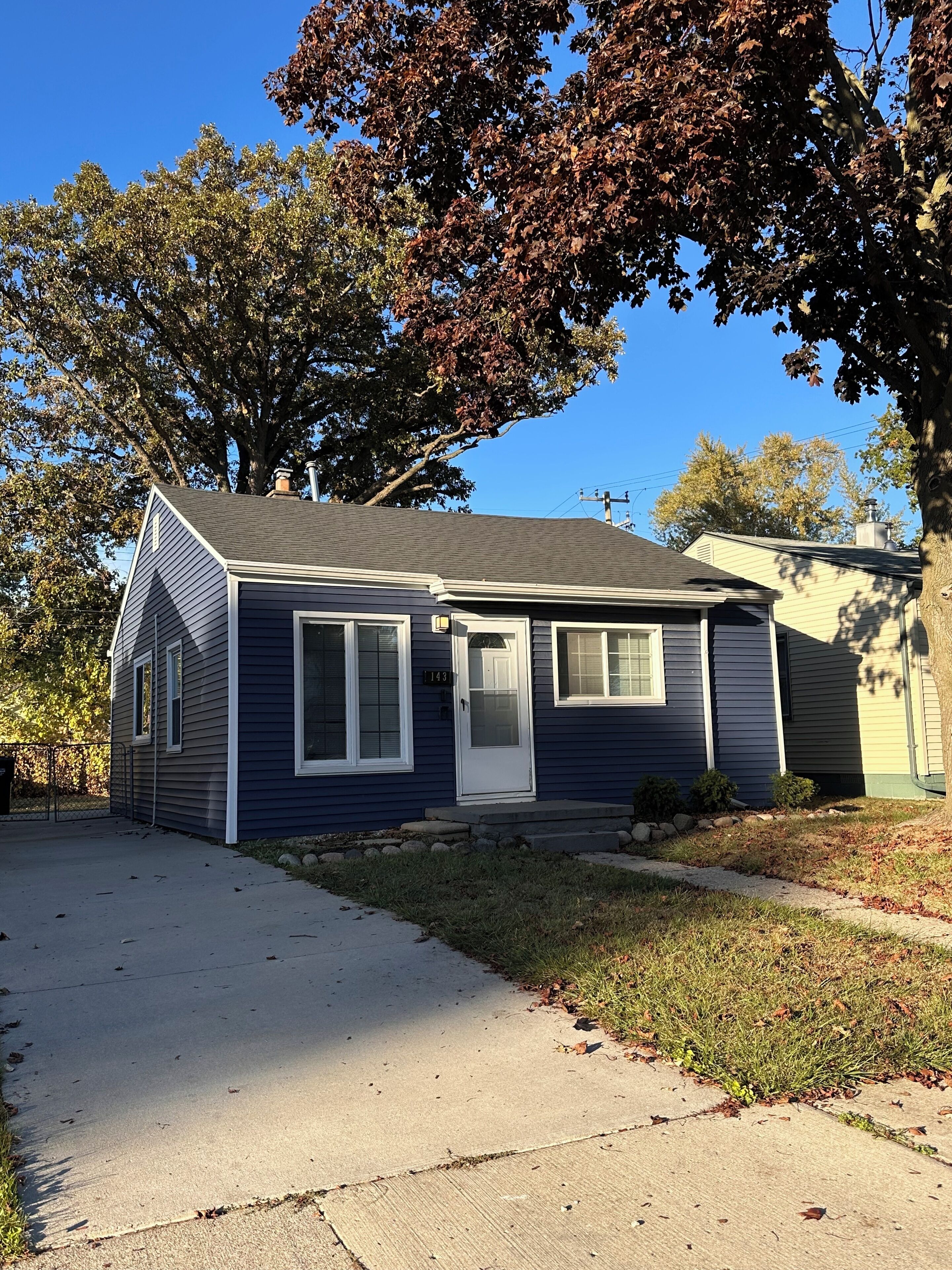 A single-story house with a dark blue exterior, a white front door, and a small front yard with a sidewalk leading to the entrance.