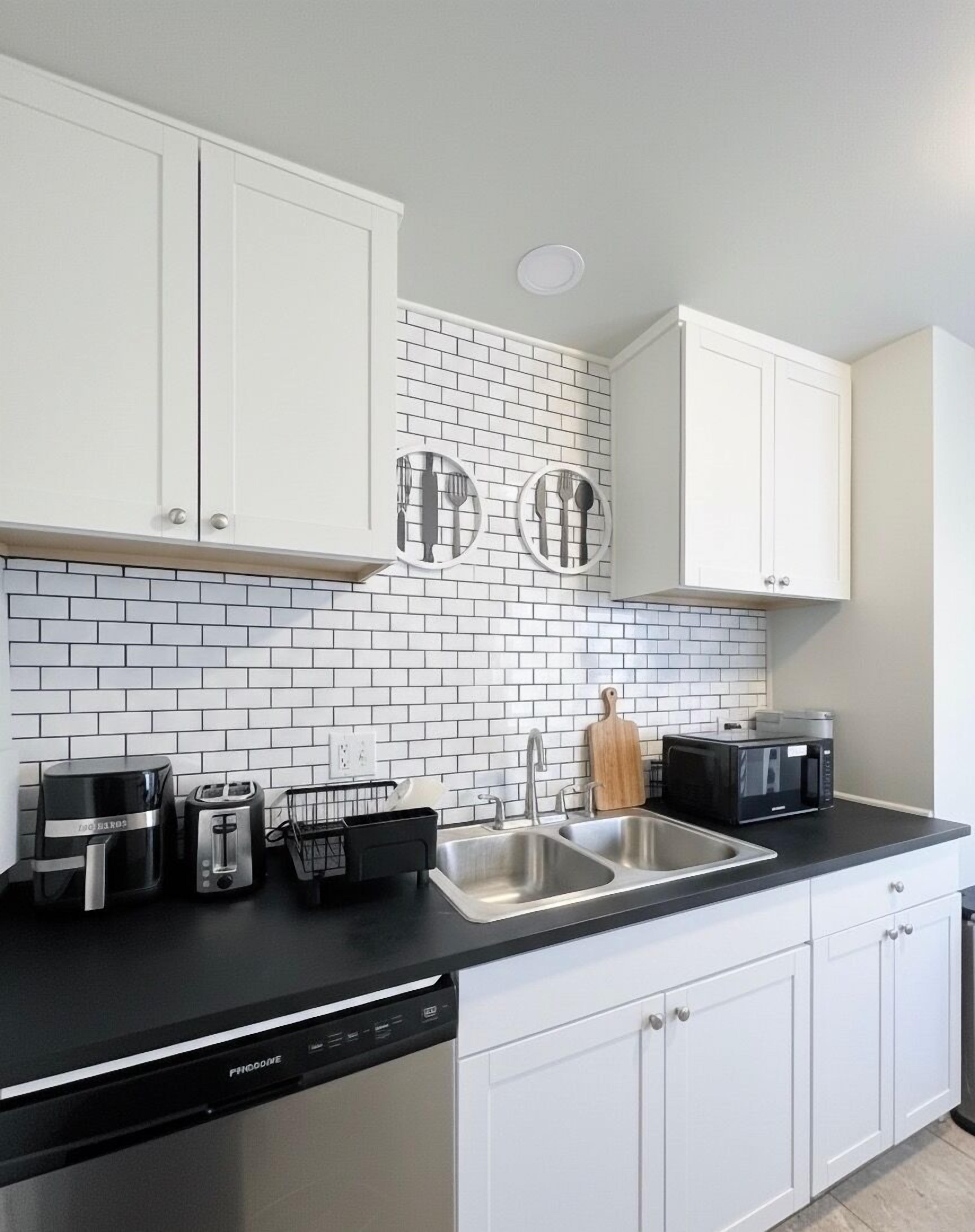 A modern kitchen with white cabinets, a black countertop, and a white-tiled backsplash.