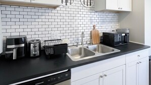 A modern kitchen with white cabinets, a black countertop, and a white-tiled backsplash. - Cozy Home in Madison Heights (Madison Heights)