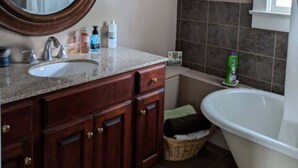 A bathroom with a wooden vanity, a round mirror, a white sink, and a white bathtub. - Gate House (2 Doubles + 1 Single - 2nd Floor) (Lancaster)