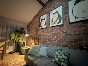 Una sala de estar acogedora con una pared de ladrillo, un sofá gris y dos cuadros enmarcados que representan pájaros.