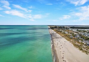 A coastal beach with clear turquoise waters, a sandy shore, and a row of buildings along the coastline. - Private Pool Home In Wellen Park - golf included - Links & Leisure (Venice)