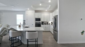 Une cuisine moderne avec des meubles blancs, un îlot central doté de tabourets, un four encastré et un réfrigérateur en acier inoxydable.