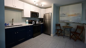 A modern kitchen with white cabinets, a stainless steel refrigerator, a microwave, and a coffee maker. There is a small table with two chairs and a painting on the wall. - Lovely king room in 8 unit Inn in tranquil Sanibel with bikes, beach gear... (Sanibel)