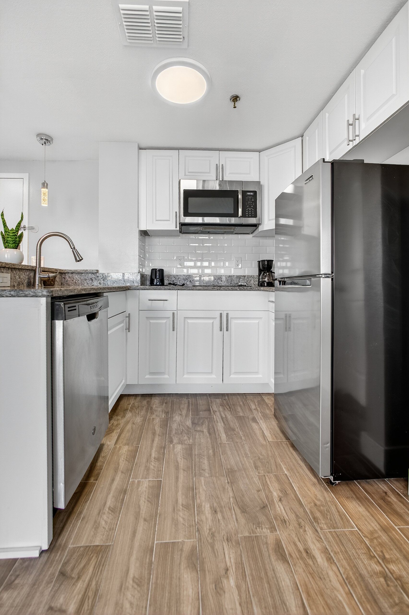 A modern kitchen with white cabinets, stainless steel appliances, and a wooden floor.