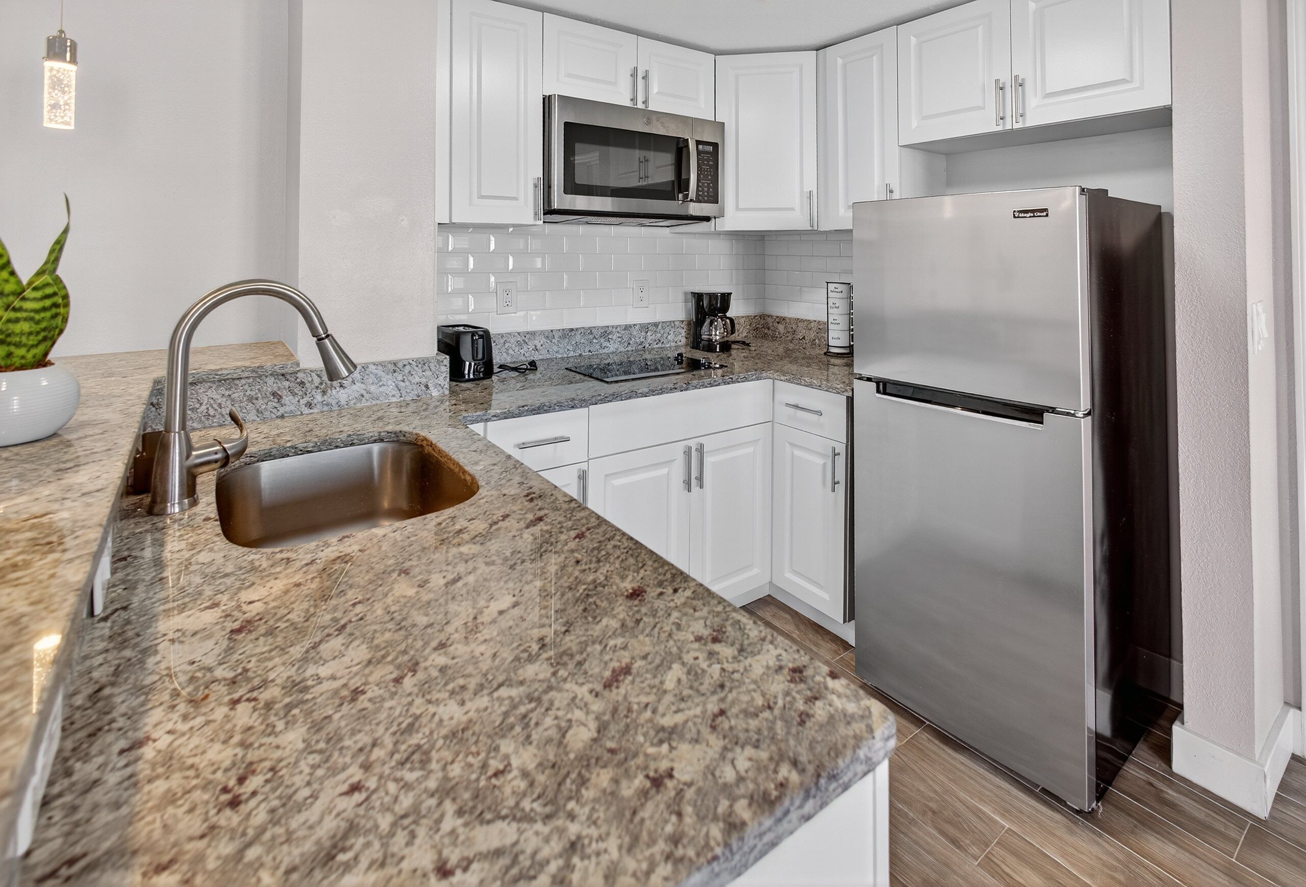 A modern kitchen with white cabinets, a stainless steel refrigerator, a built-in microwave, and a granite countertop.