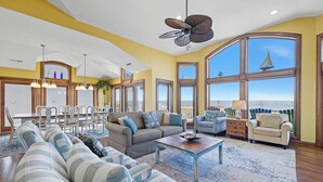 A spacious living room with a large window offering a view of the ocean, a dining area with a high ceiling, and a cozy seating area with a fireplace. - Bella Vista II | 3,144 ft to the beach | Private Pool and Hot Tub (Corolla)
