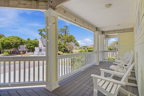 A covered porch with white railings and wooden chairs.