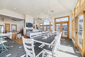 A spacious kitchen with a central island, a dining area with a long table and chairs, and large windows offering a view of the surrounding area. - Salt and Soul Cottage | 1,228 ft to the beach | Private Pool and Hot Tub (Corolla)
