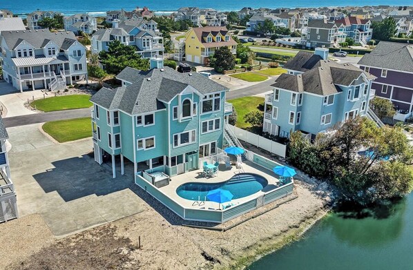 A large two-story house with a swimming pool, surrounded by other houses and a body of water. - Salt and Soul Cottage | 1,228 ft to the beach | Private Pool and Hot Tub (Corolla)