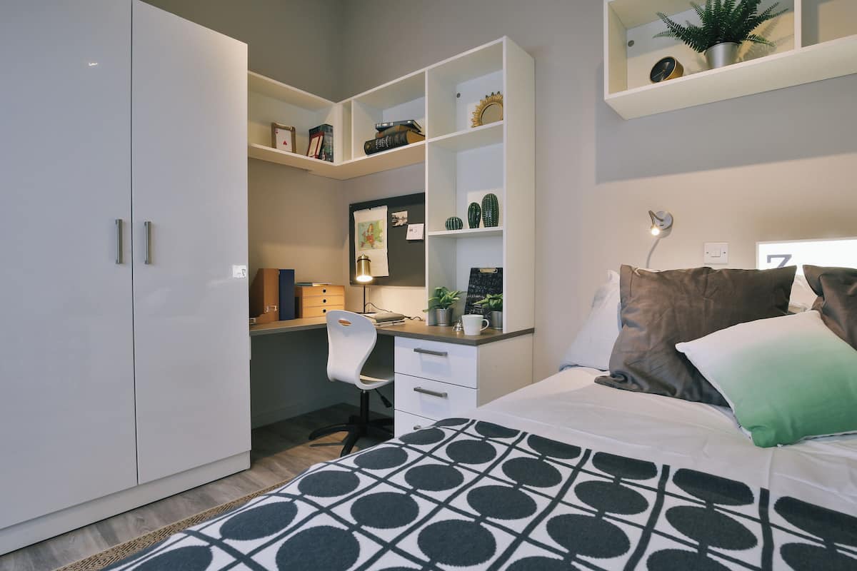 A modern bedroom with a large bed, a desk, and built-in shelving.