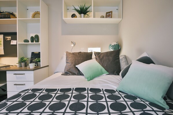 A neatly organized bedroom with a bed, pillows, a desk, and shelves with various items. - Student Only The Chapel (Manchester)