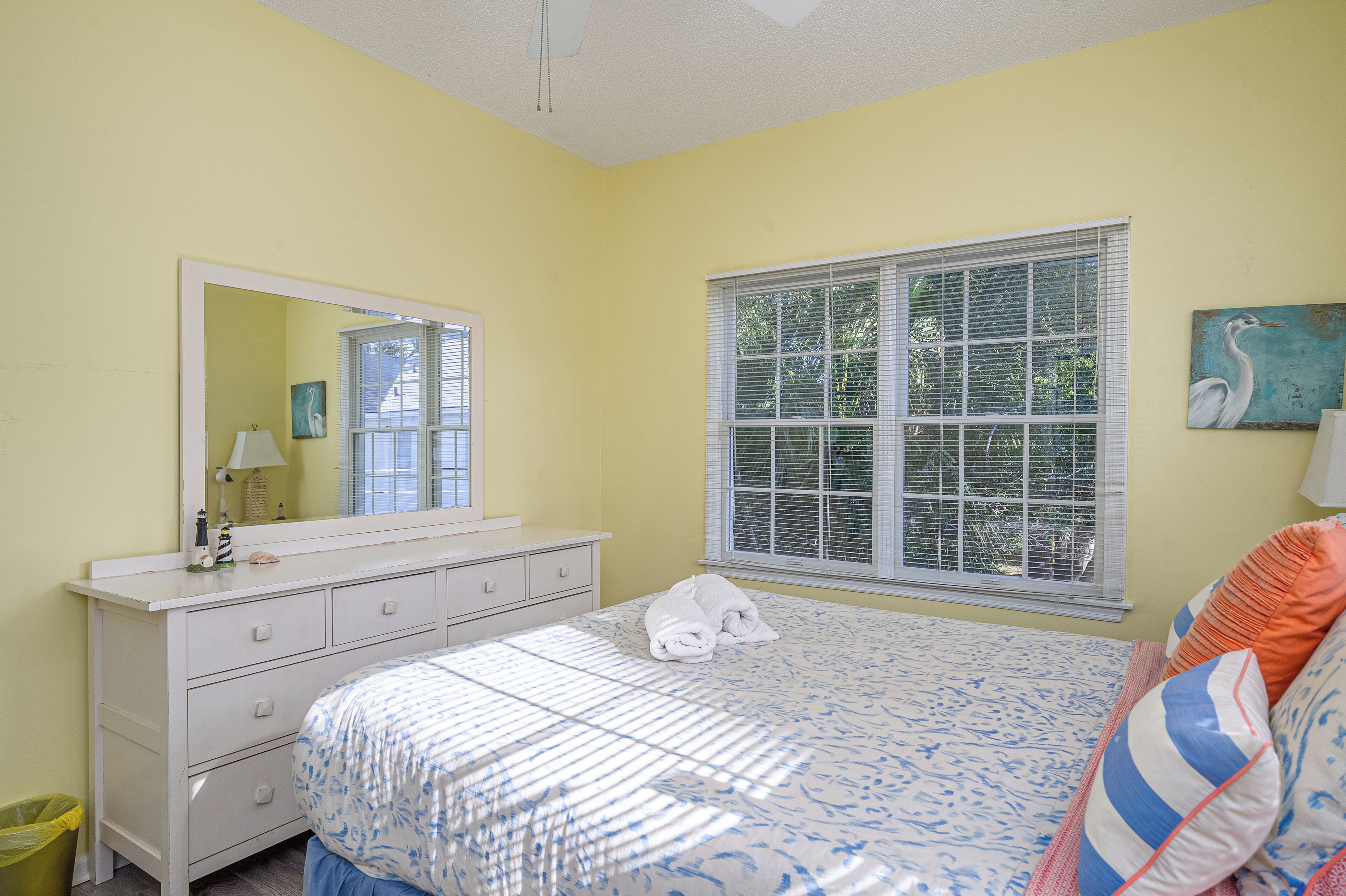 A bedroom with a bed, a dresser, a window, and a painting.