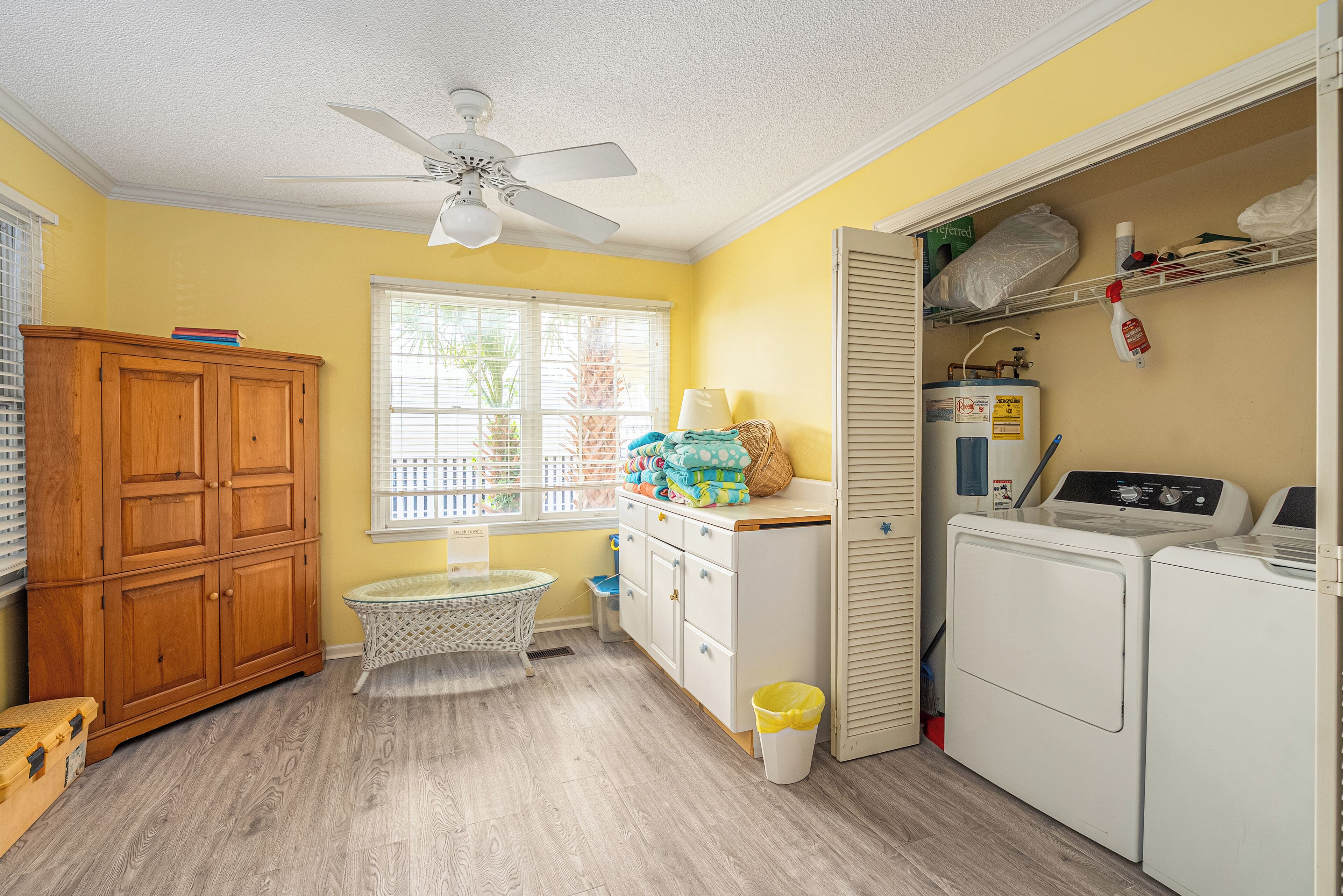 A laundry room with a ceiling fan, a washing machine, a dryer, a wooden cabinet, a laundry basket, and a window with blinds.