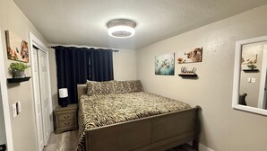 Une chambre à coucher comprenant un lit, une table de chevet, une lampe, un luminaire au plafond, une porte, un miroir et des œuvres d’art murales.