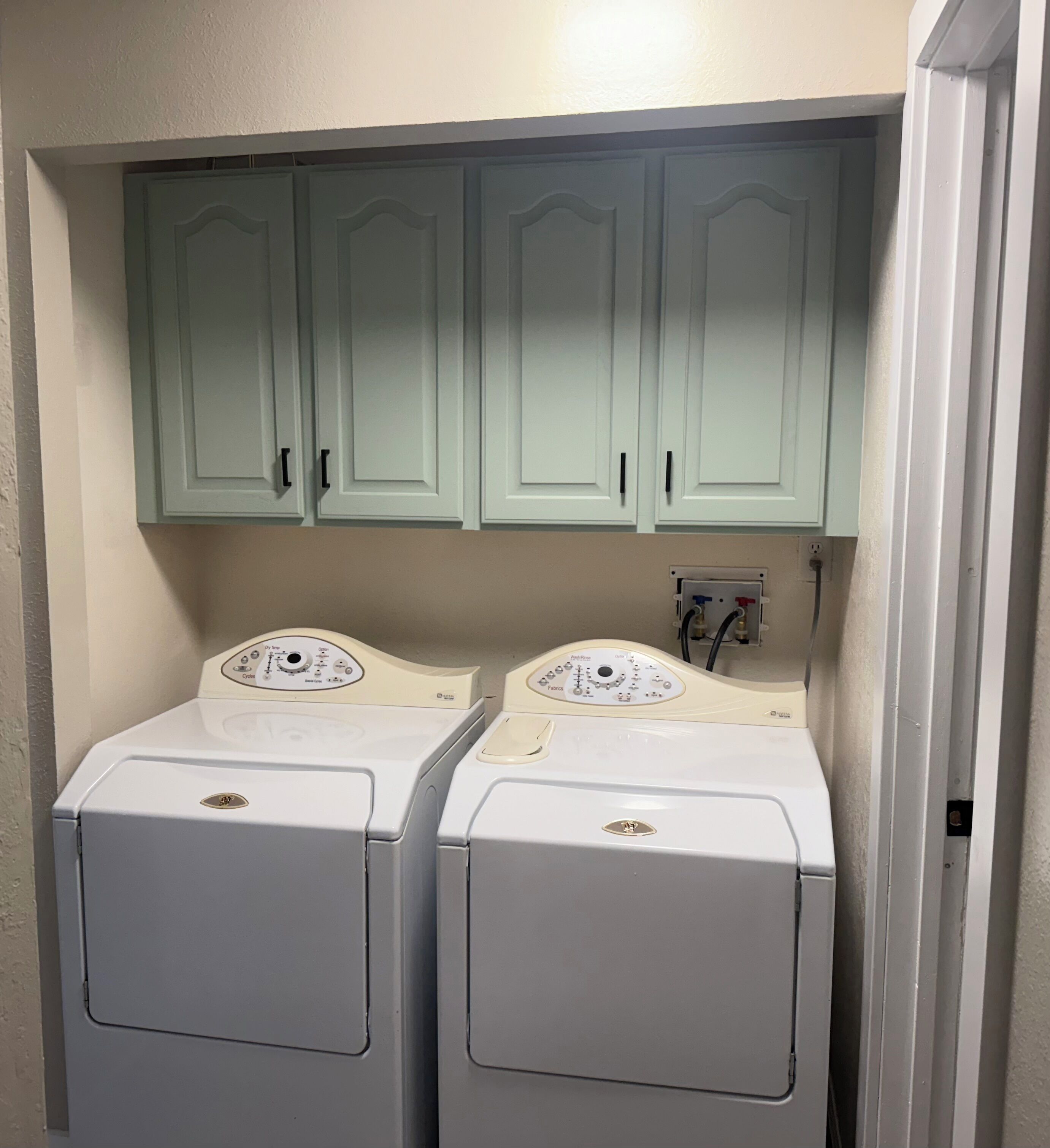 A laundry room with two front-loading washing machines and a control panel above them.