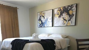 Une chambre d’hôtel avec un lit, une chaise et deux tableaux abstraits accrochés au mur.