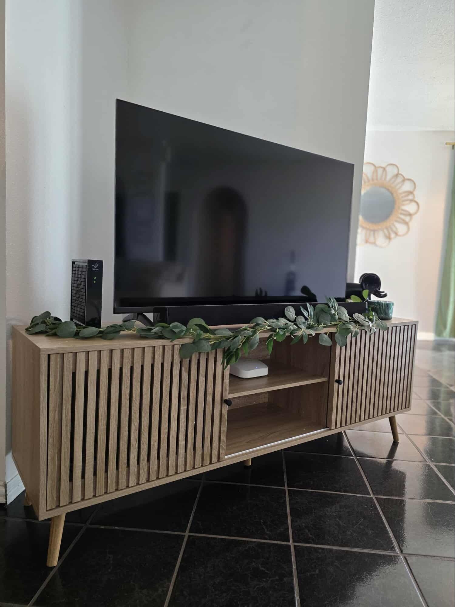 A wooden TV stand with a flat-screen TV, a decorative plant, and a small statue.