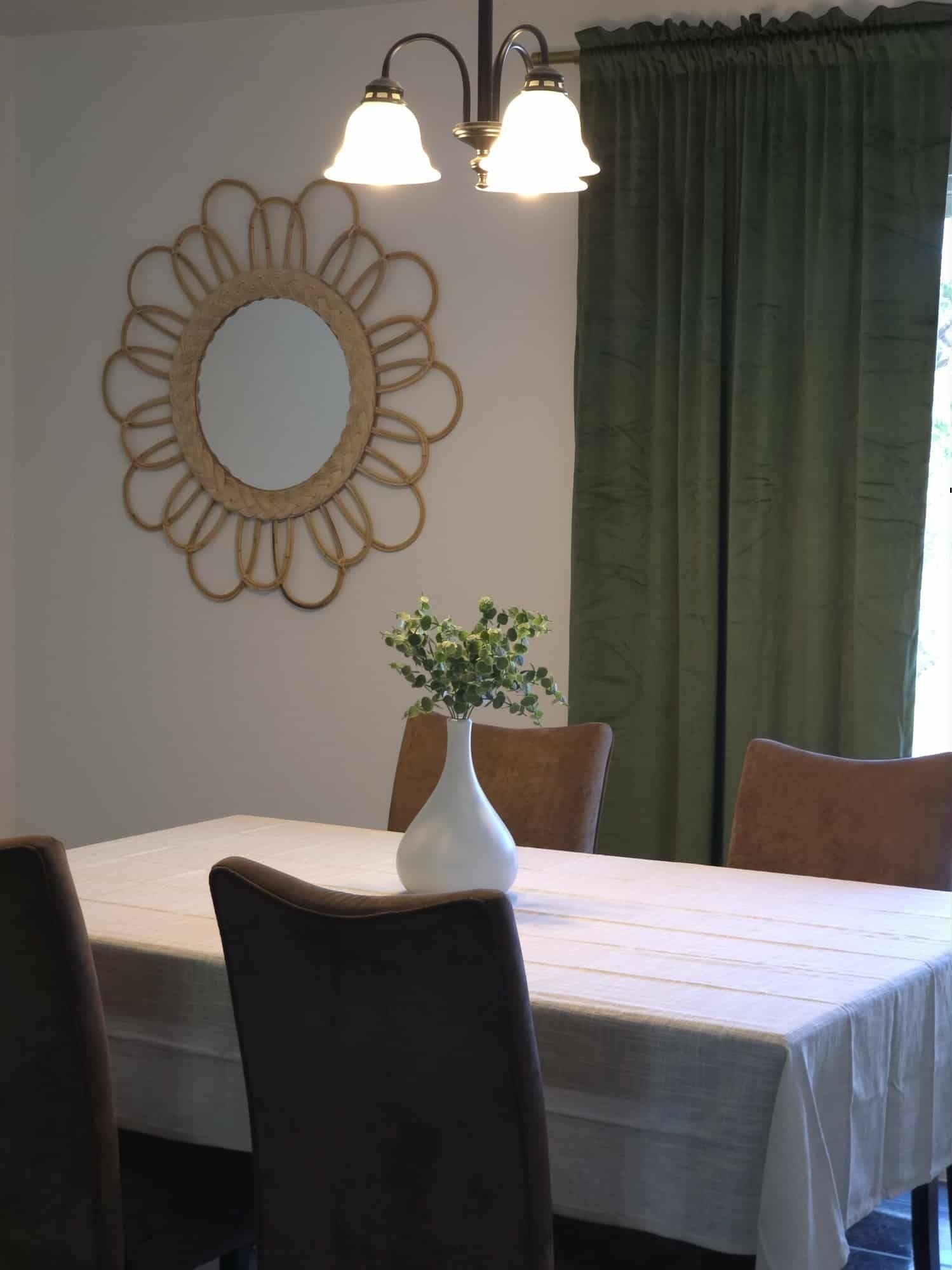 Un coin repas avec une table dressée pour quatre personnes, un miroir décoratif et un vase avec une plante.