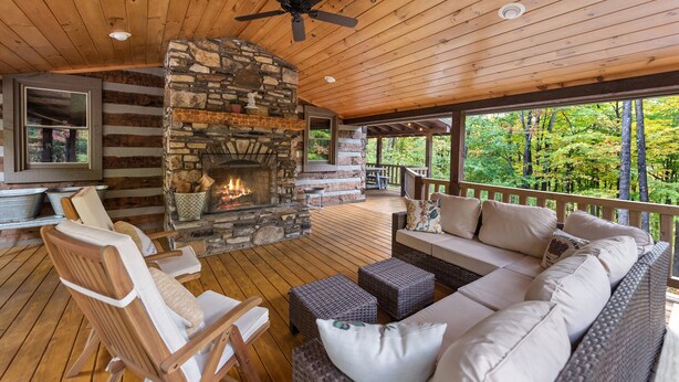 Une terrasse en bois avec un foyer en pierre, des sièges d’extérieur et un téléviseur fixé au mur.