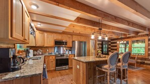 Une cuisine spacieuse dotée de meubles en bois, d’appareils électroménagers en acier inoxydable et d’un îlot central agrémenté de tabourets de bar.