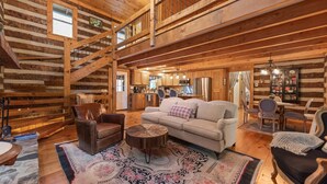 Un intérieur spacieux de chalet en bois, comprenant un salon, un coin repas, une cuisine et un escalier menant à un niveau supérieur.