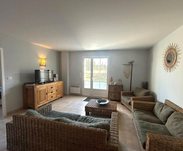 Un salón amplio con muebles de mimbre, un televisor y un adorno de pared.