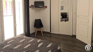A room with a bed, a chair, a TV on a shelf, a wardrobe, and a door.