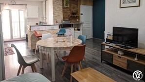 A modern kitchen with a central island, a dining area with a round table, and a living area with a TV and wooden furniture.