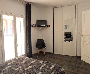 Een kamer met een bed, een stoel, een televisie op een plank, een kledingkast en een deur.