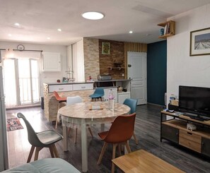 Een moderne keuken met een centraal eiland, een eetgedeelte met een ronde tafel, en een zithoek met een televisie en houten meubels.