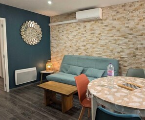 Een moderne woonkamer met een wand met steenmotief, een blauwe bank, een houten salontafel en een ronde tafel met stoelen.