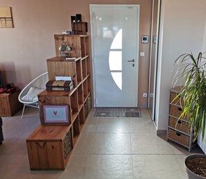 Ein Flur mit einer hölzernen Bank, einem weißen Stuhl, einer Holzregaleinheit und einem Blumentopf.