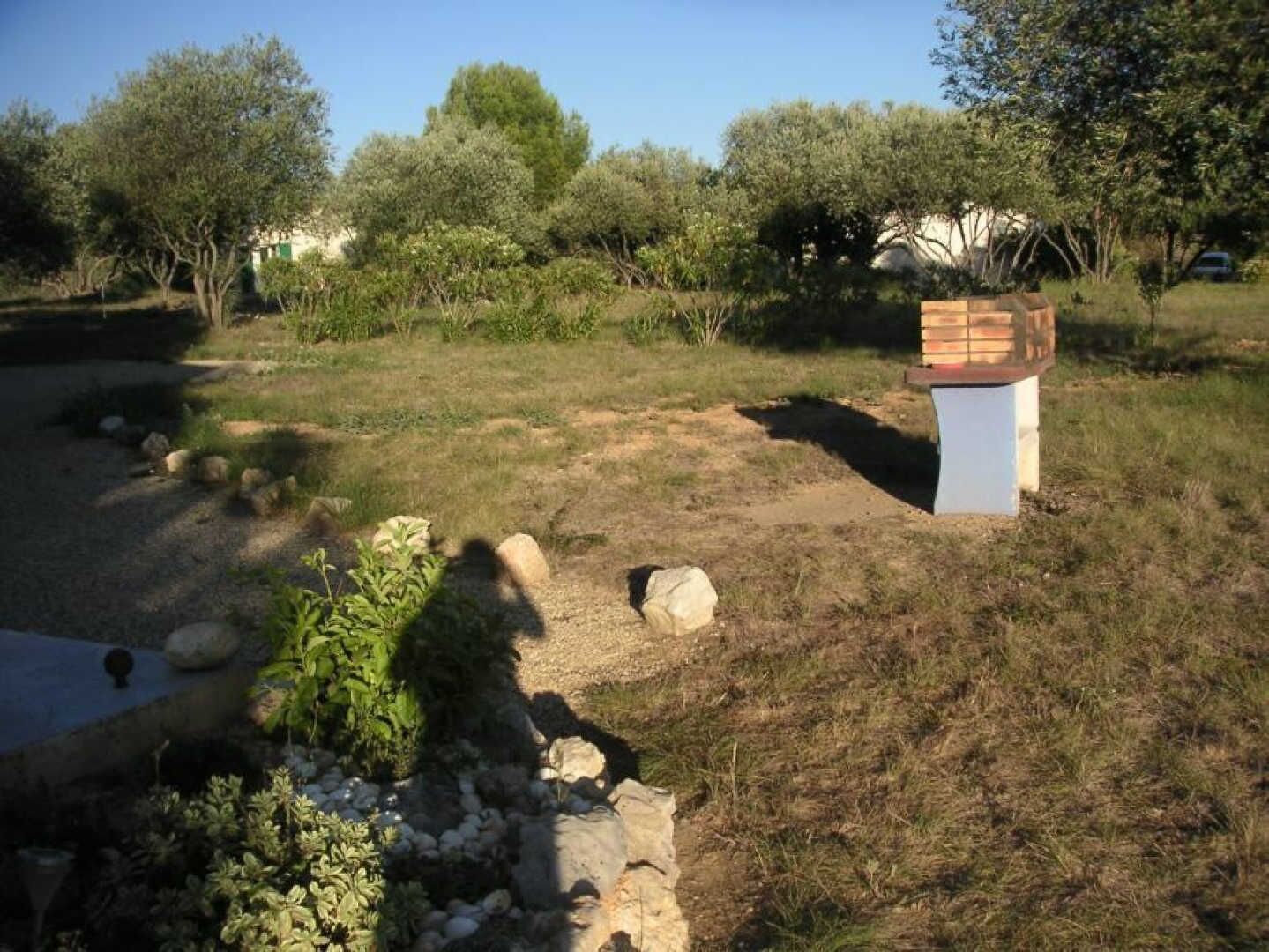 Un jardin avec un chemin de pierres, des rochers et une structure blanche surmontée d’un toit brun.