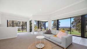 A spacious living room with a grey sofa, a round coffee table, and large windows offering a view of the outdoors.