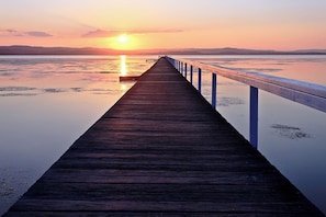 A wooden pier extending into calm water with a sunset in the background.