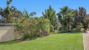 A well-maintained lawn with a variety of tropical plants and a wooden fence.