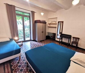 Quarto com duas camas, uma escrivaninha, uma cadeira, um guarda-roupa e uma janela com cortinas.
