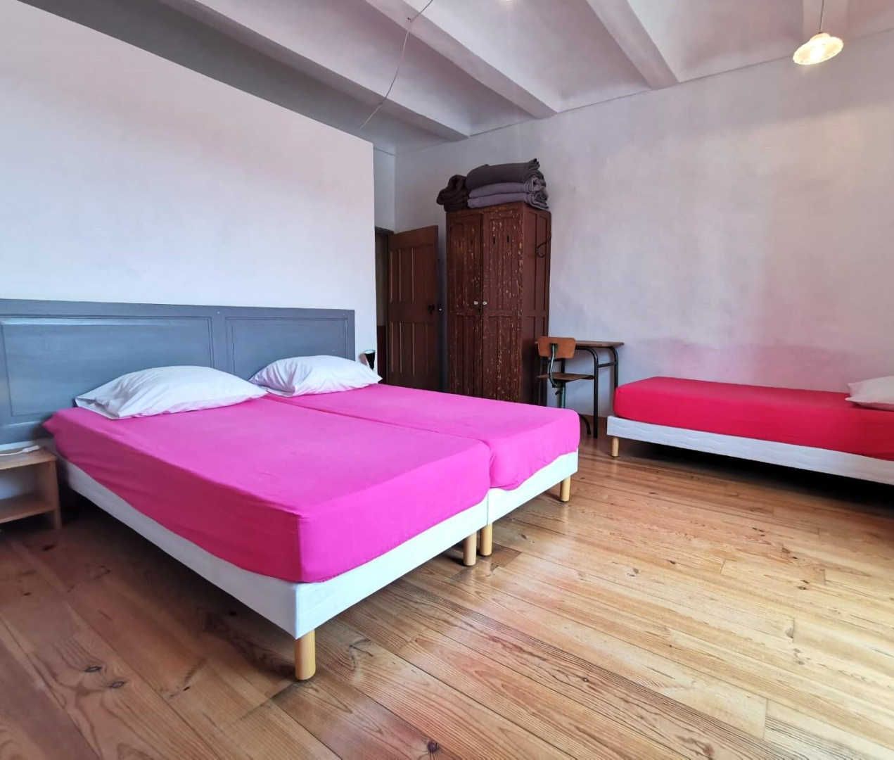 A room with two beds, wooden flooring, a desk, and a wardrobe.