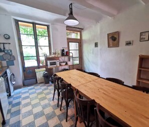 Uma cozinha com mesa e cadeiras de madeira, micro-ondas e pia. H á janelas e um ventilador de teto.