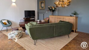 A modern living room with a green sofa, a wooden cabinet, a television, and decorative wall art. - Ferme les Taillades 2-4 persons (CAMBON ET SALVERGUES)