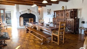 A spacious room with a wooden floor, a fireplace, a dining table with benches, and a large wooden cabinet. - Ferme les Taillades 2-4 persons (CAMBON ET SALVERGUES)