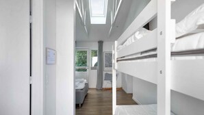 A modern, well-lit room with bunk beds, a small seating area, and a window with a view of greenery. - 5 Star Holiday Home in Svaneke (Svaneke)