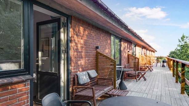 A covered outdoor seating area with brick walls, wooden furniture, and a wooden deck. - 5 Star Holiday Home in Svaneke (Svaneke)