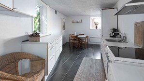 A compact kitchen with a dining area, white cabinetry, a wicker chair, and a small dining table. - 5 Star Holiday Home in Svaneke (Svaneke)