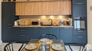 A modern kitchen with dark cabinets, a wooden countertop, and a dining area with a table set for two. - L'Arcolan - VALRAS PLAGE (VALRAS PLAGE)